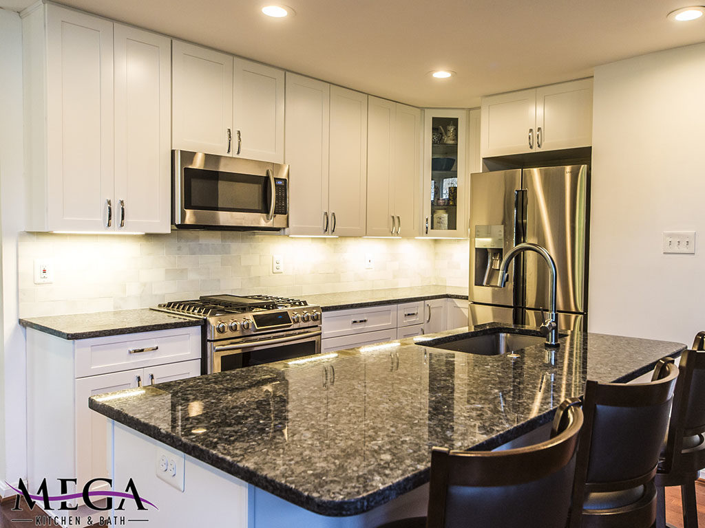 Luxury, medium sized kitchen with white shaker cabinets and black countertops