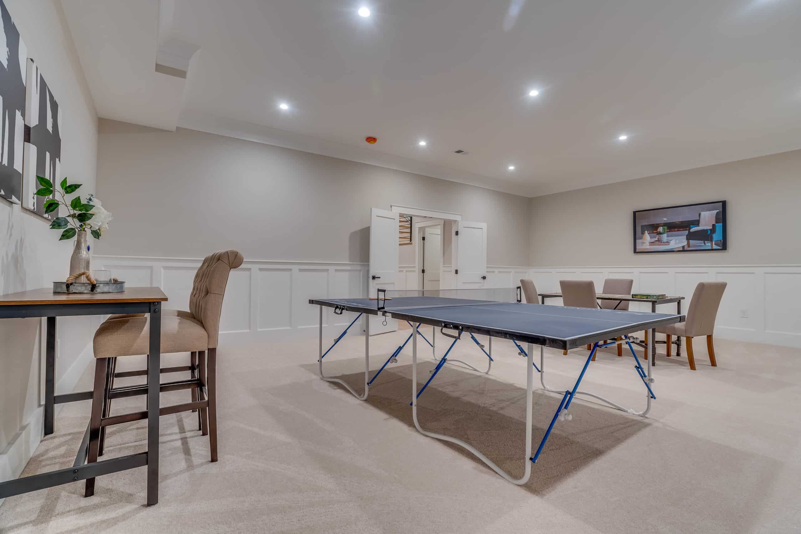 Open area in basement with table tennis, dining table, TV, and side table.