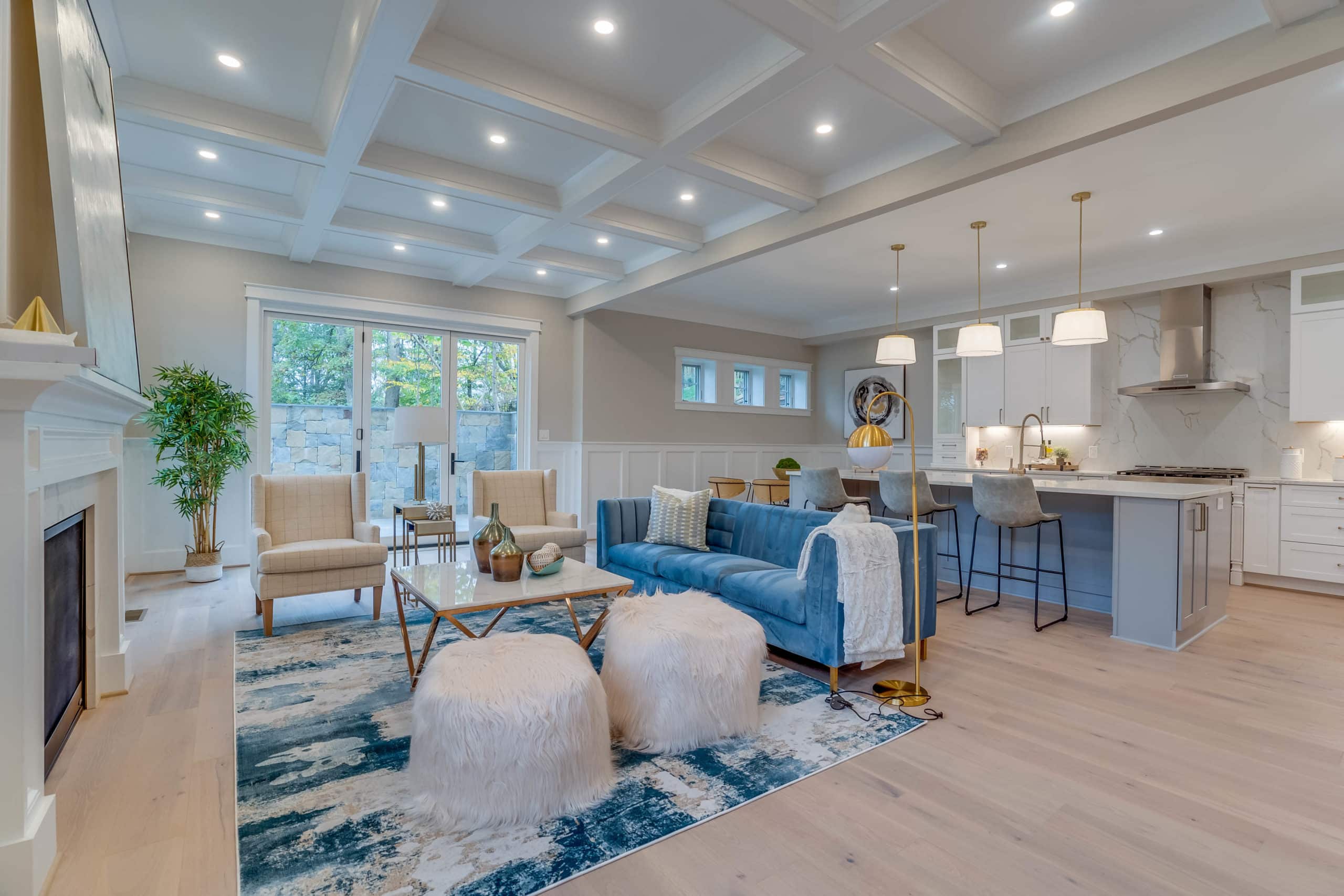 Luxurious living room and kitchen with light oak flooring, white shaker cabinets, white and blue sofa, and high ceiling