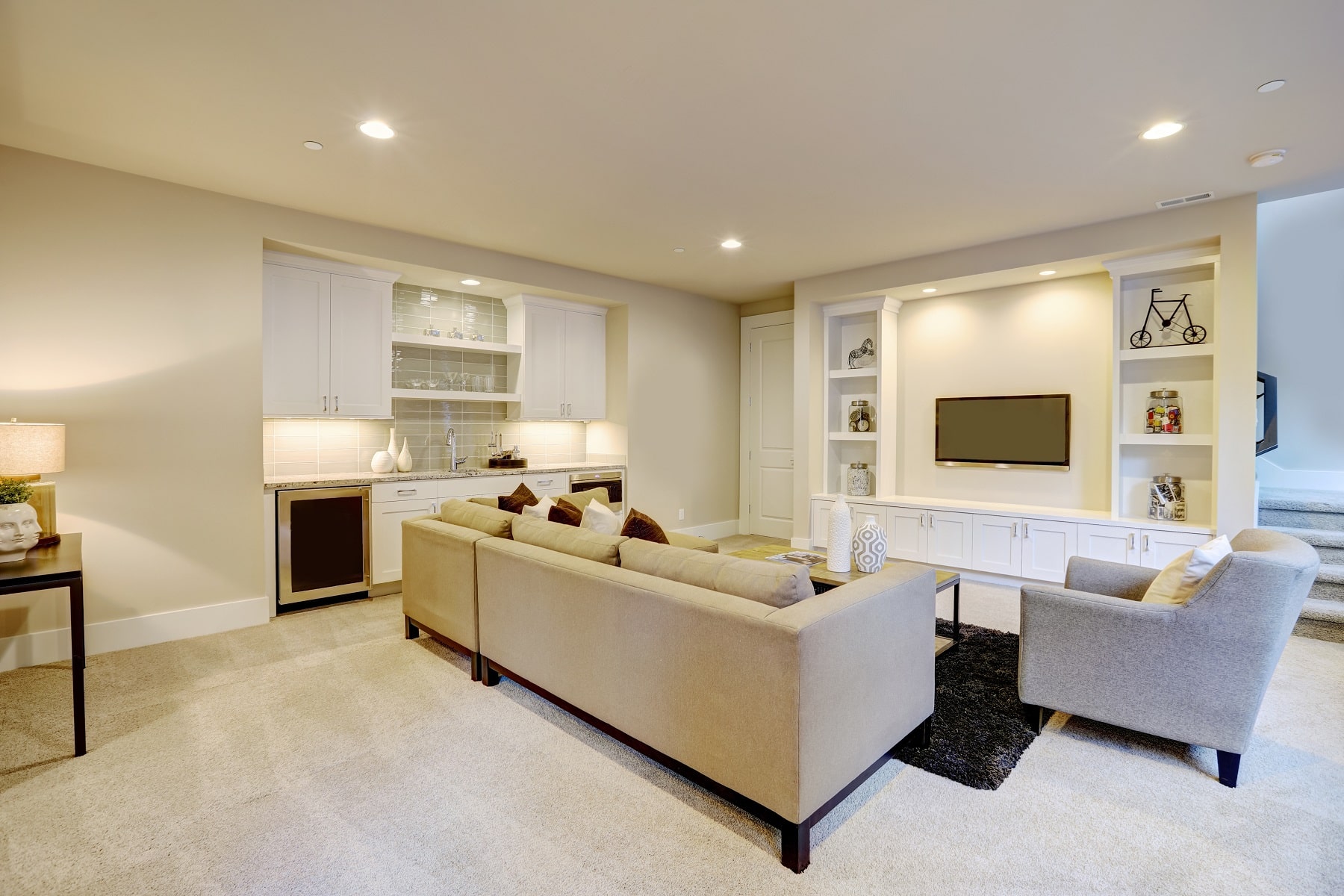 Chic basement features a gray sectional facing a white built-in tv cabinet and wet bar mounted to a wall. Northwest, USA