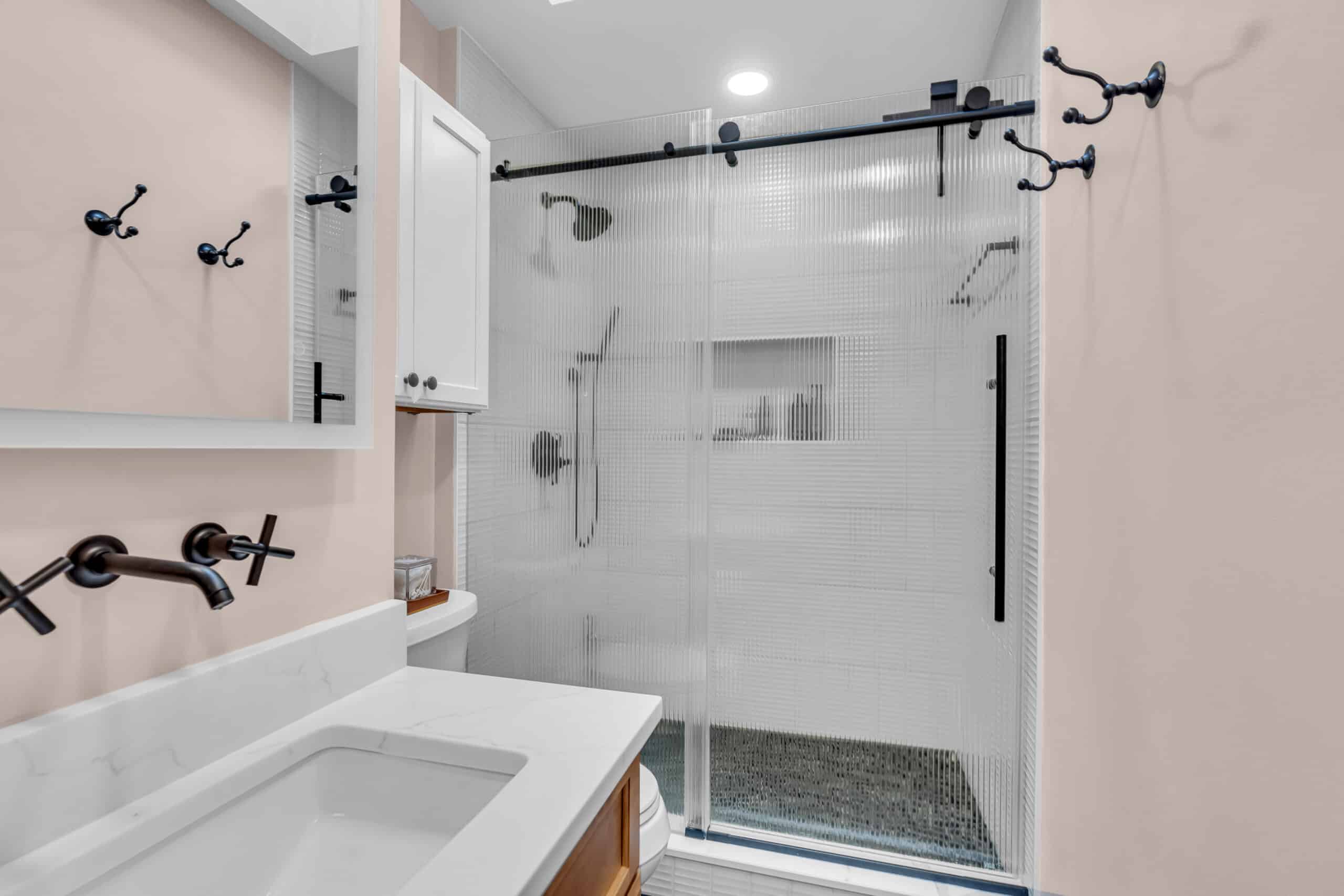 Beige bathroom with brown vanity, black hardware, and a shower