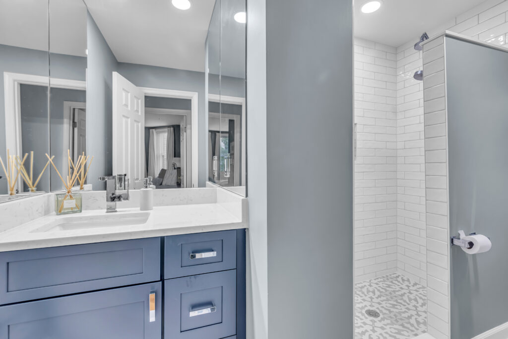 Grey bathroom design with navy blue shaker vanity, and a shower