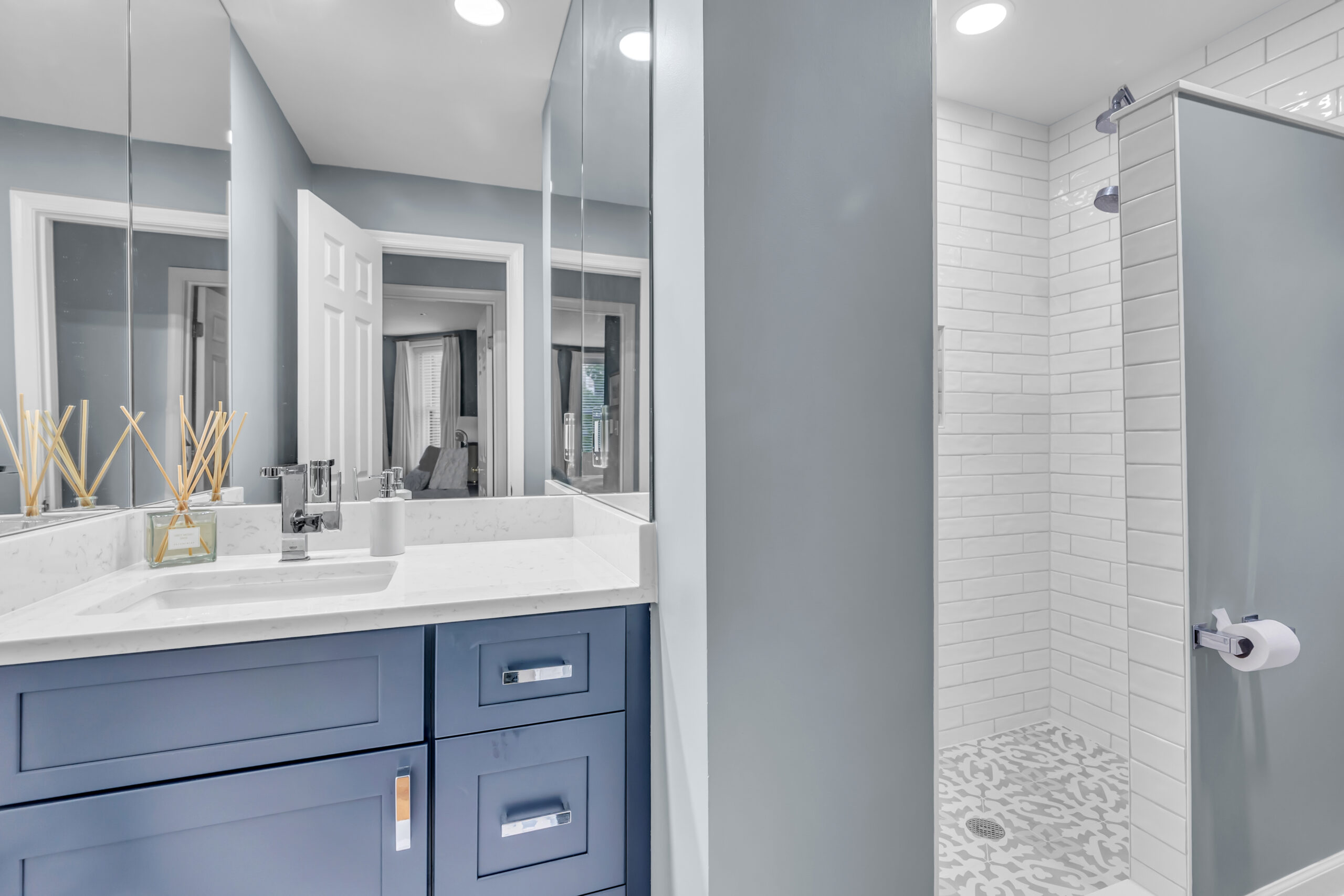 Grey bathroom design with navy blue shaker vanity, and a shower