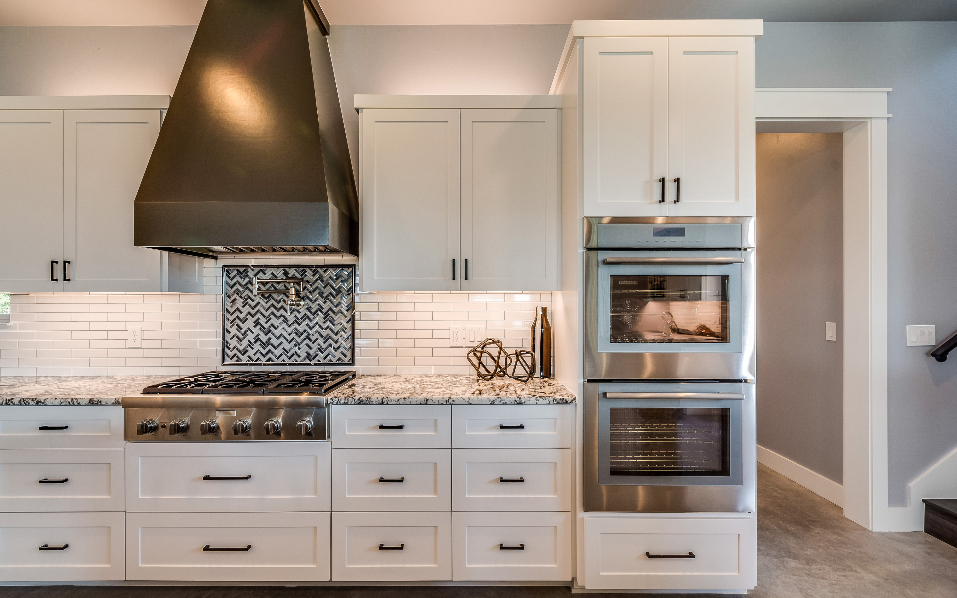 Elegant kitchen with white cabinets, and bronze range hood